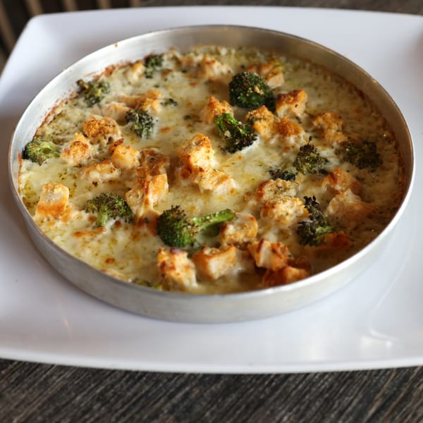 A Milano's Pizzeria dish with melted cheese, chicken, and broccoli in a metal pan.