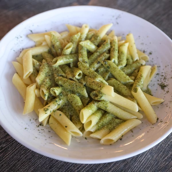 Penne pasta with green pesto sauce and herbs on a white plate at Milano's Pizzeria.