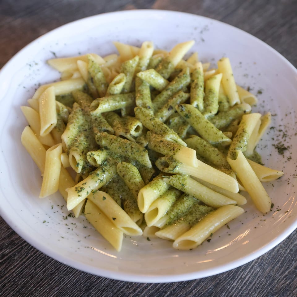 Penne pasta with green pesto sauce and herbs on a white plate at Milano's Pizzeria.