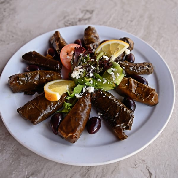 Grape leaves, olives, lemon, tomato, and feta cheese salad on a white plate.