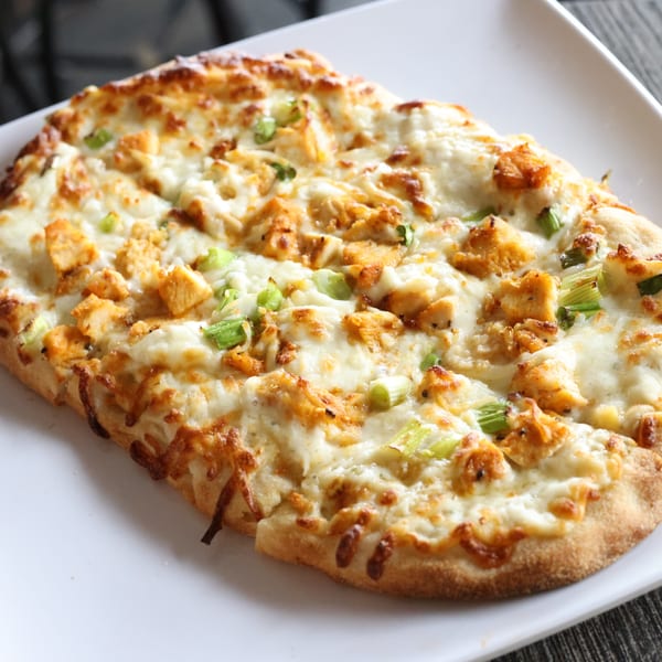 Milano's Pizzeria's chicken flatbread pizza, topped with melted cheese and green onions, on a white plate.
