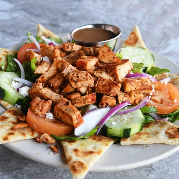 Chicken salad with lettuce, tomatoes, cucumbers, red onions, feta, and pita bread.