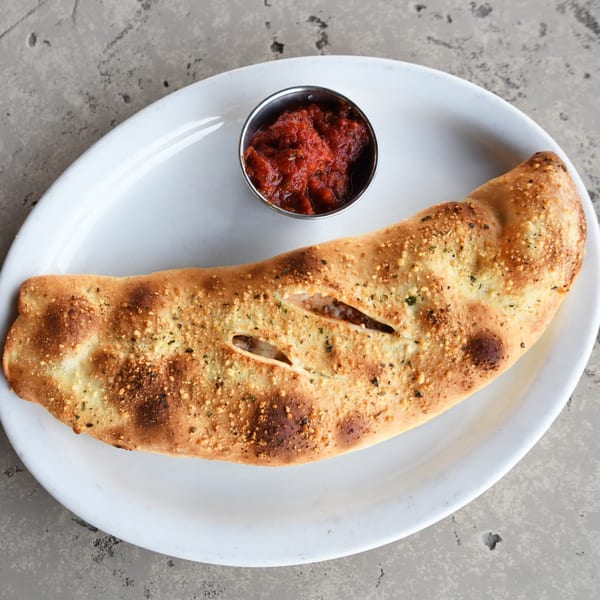 A golden-brown Milano's Pizzeria calzone with visible cheese and sauce, served with a side of marinara.