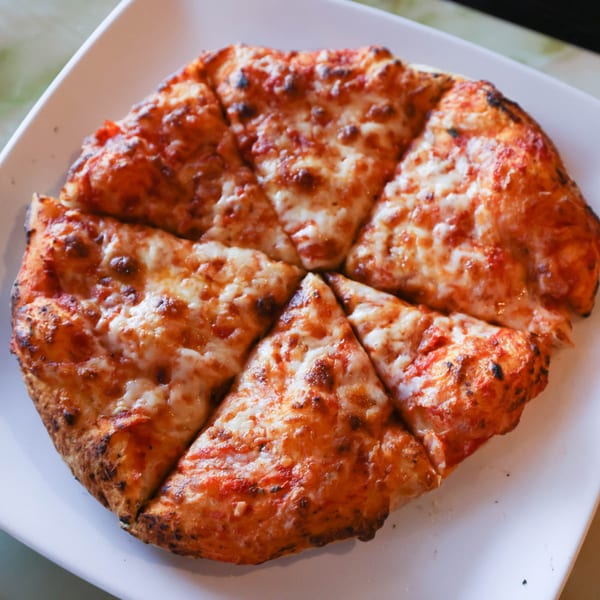 A Milano's Pizzeria cheese pizza, cut into six slices, on a white plate.